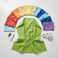 On the Go Leaves Green quilting cotton by Jason Yenter for In The Beginning Fabrics — draped as the hero in the center of a rainbow fan spread of coordinating fabrics, with a green thread spool, gold scissors, and a small toy bicycle on a white surface. Coordinating fabrics and quilt patterns available at IraRobi Quilts.