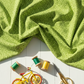 On the Go Leaves Green quilting cotton by Jason Yenter for In The Beginning Fabrics — vertical lifestyle photo with the tone-on-tone leaf print fabric draped as the hero on a white wood surface, with green and yellow thread spools, gold scissors, and a yellow toy bicycle below. Coordinating fabrics and quilt patterns available at IraRobi Quilts.
