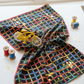 On the Go Plaid Multi quilting cotton by Jason Yenter for In The Beginning Fabrics — vertical lifestyle photo with the bold rainbow grid on black as the hero, styled with a yellow toy bicycle, gold star confetti, and colorful wood thread spools. Coordinating fabrics and quilt patterns available at IraRobi Quilts.