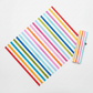 On the Go Stripes Multi quilting cotton by Jason Yenter for In The Beginning Fabrics — flat lay showing fabric cut on the diagonal to demonstrate the dynamic chevron bias effect, with a folded binding strip alongside on a white surface.