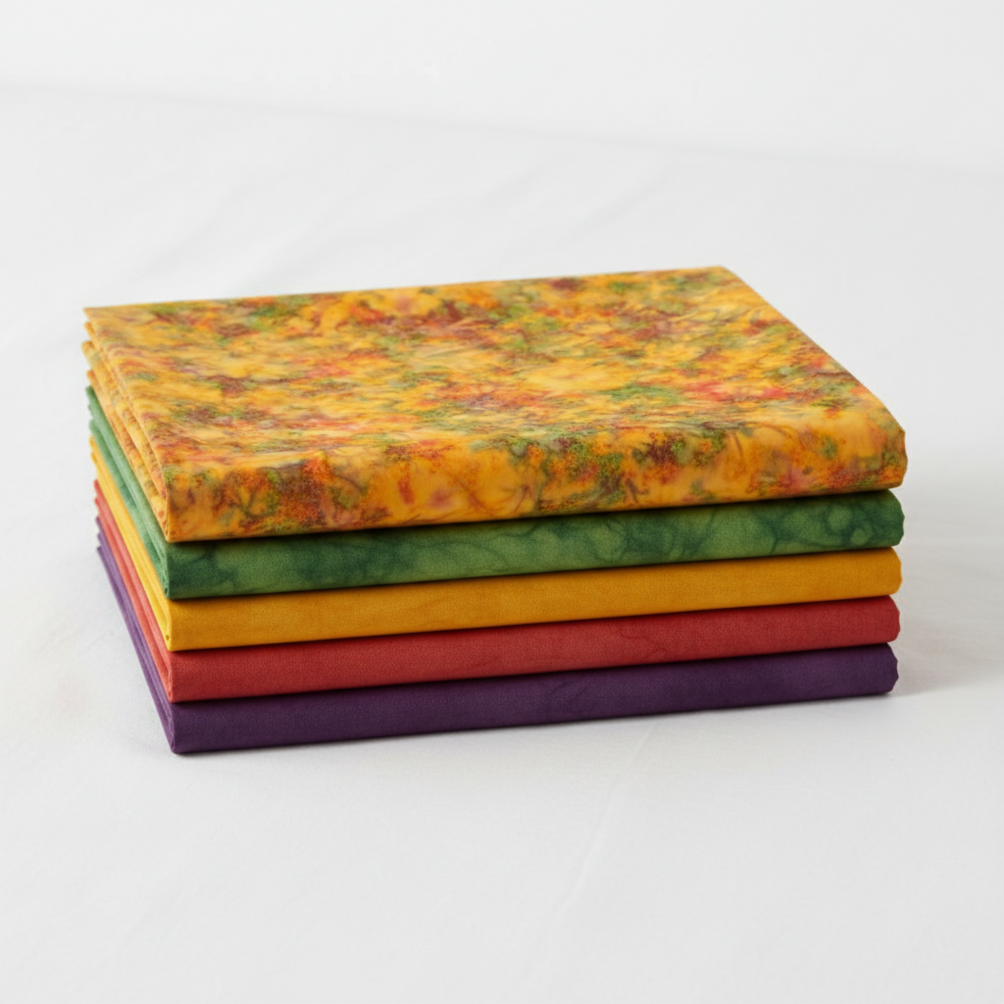 Expressions Batiks Hand-Dyes Orange Multi II fabric by Riley Blake Designs on top of a coordinating stack of five Expressions Batiks Hand-Dyes tonal batik fabrics – bright luminous golden amber-orange multicolor on top with forest green, curry yellow, tomato red, and deep purple tonal batiks below, 100% cotton