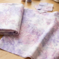 Color Play Mottled Lilac Lustre fabric by Riley Blake Designs, folded and draped across a sewing table with matching remnants, pink and lavender thread, a pincushion, and a sewing machine.