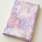 Neatly folded Color Play Mottled Lilac Lustre fabric by Riley Blake Designs on an ivory surface, showing pale pink and lavender mottling.
