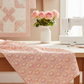 Patricia Coral Lace 3-Yard Cut quilting cotton by Jason Yenter for In The Beginning Fabrics — draped in the foreground of a bright romantic quilting studio with a soft blush and ivory patchwork quilt, white sewing machine, and vase of pink roses in the background. Coordinating fabrics and quilt patterns are available at IraRobi Quilts.