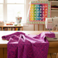 PAWsitivity Purple Field 3 Yard Cut quilting cotton by Jason Yenter for In The Beginning Fabrics — featured as the hero fabric draped in the foreground of a bright natural-light quilting studio, with a colorful rainbow PAWsitivity half-square triangle quilt and Bernina sewing machine softly visible behind. Quilts shown for inspiration feature the ModCat Quilt Pattern by Colourwerx — available at IraRobi Quilts.