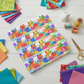 PAWsitivity White Border Stripe quilting cotton by Jason Yenter for In The Beginning Fabrics — folded flat on a white wooden surface surrounded by colorful pinking-sheared fabric swatches in rainbow and jewel tones, wooden thread spools, gold scissors, and a ceramic cat figurine in a bright cheerful sewing room flat lay