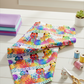 PAWsitivity White Border Stripe quilting cotton by Jason Yenter for In The Beginning Fabrics — loosely draped on a white wooden surface with coordinating PAWsitivity fabrics in purple, teal, and rainbow tones, rainbow thread spools, gold scissors, and a ceramic cat figurine in a bright natural-light quilting room. Coordinating fabrics and quilt patterns are available at IraRobi Quilts.