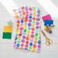 PAWsitivity White Flower Stripe quilting cotton by Jason Yenter for In The Beginning Fabrics — loosely draped on a white wooden surface with coordinating rainbow fabric swatches, rainbow thread spools, gold scissors, and a white ceramic cat figurine in a bright cheerful sewing room flat lay.