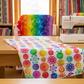 PAWsitivity White Flower Stripe quilting cotton by Jason Yenter for In The Beginning Fabrics — draped in the foreground of a bright quilting studio with a colorful rainbow jewel-tone quilt, Bernina sewing machine, rotary cutter, cutting mat, and shelves of fabric bolts in the background. Coordinating fabrics and quilt patterns are available at IraRobi Quilts.