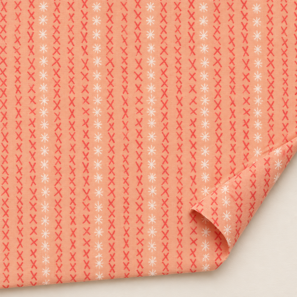 Dandi Duo Peach fabric laid flat with a folded corner, showing its coral stitched-X rows and white starbursts.