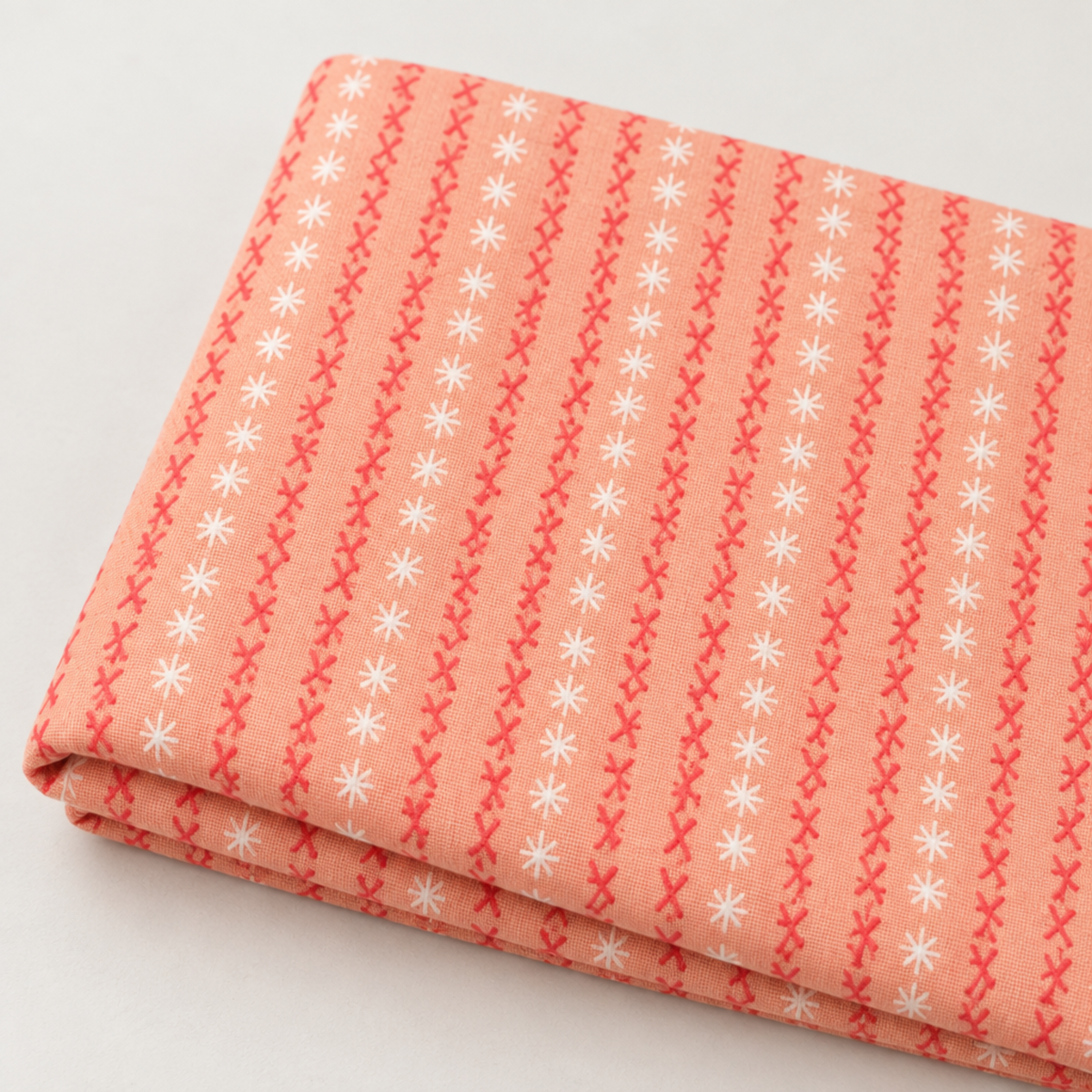Close view of folded Dandi Duo Peach fabric with coral stitched-X rows and tiny white starbursts.