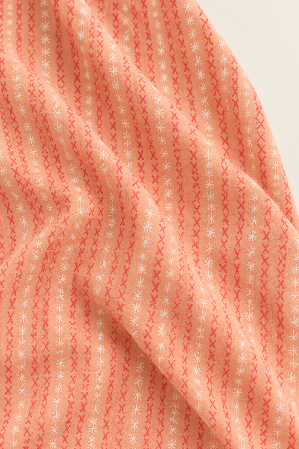 Folded Dandi Duo Peach fabric showing coral stitched-X rows and white starbursts on peach.