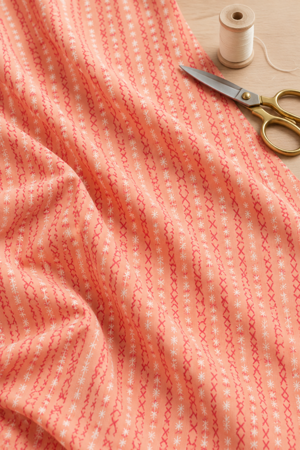 Dandi Duo Peach fabric draped on a sewing table beside a thread spool and scissors.