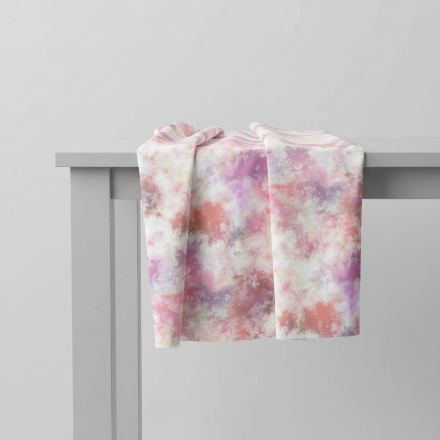 Fire & Ice by Maywood Studio Peach Ice Dye cotton quilting fabric folded and draped over a light grey table edge showing natural folds and texture