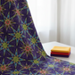 What If Radio Star Purple/Multi by Paula Nadelstern for Benartex draped elegantly showing full kaleidoscopic starburst repeat, with coordinating Interwoven fabric fat quarters in yellow, red, and purple