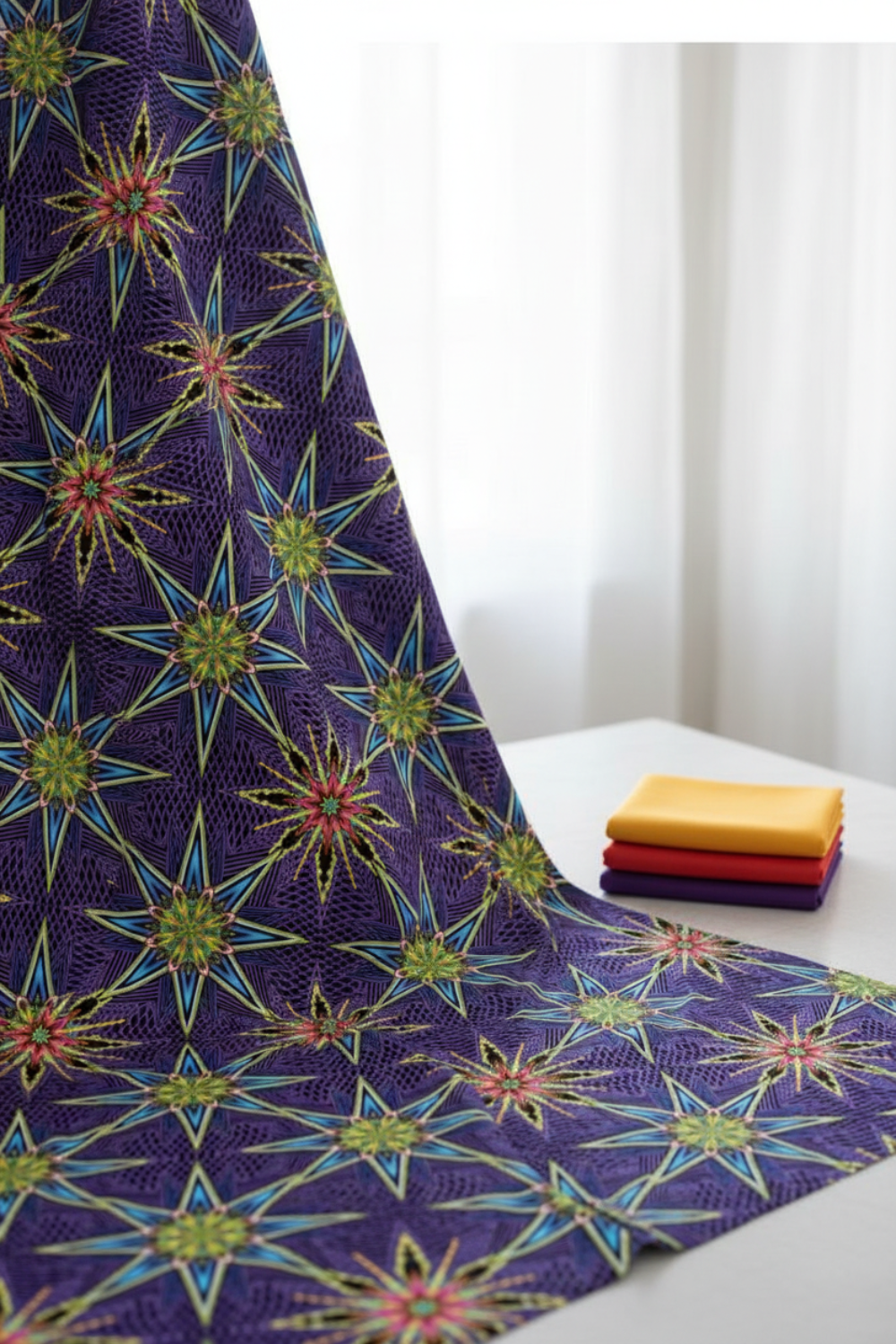 What If Radio Star Purple/Multi by Paula Nadelstern for Benartex draped elegantly showing full kaleidoscopic starburst repeat, with coordinating Interwoven fabric fat quarters in yellow, red, and purple