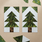 Quilting work-in-progress flat lay showing two Pine Tree quilt blocks pieced with Expressions Batiks Hand-Dyes Amazon fabric by Riley Blake Designs – rich jungle green hand-dyed batik with golden-yellow undertones in stacked triangle tiers on a light icy blue-grey batik background, with loose cut fabric pieces scattered on a warm linen surface