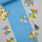 Safari Fun Floating Triangles Blue by Terry Runyan for Benartex – rolled fabric with coordinating pinwheel and star quilt blocks in progress, scissors, light grey background