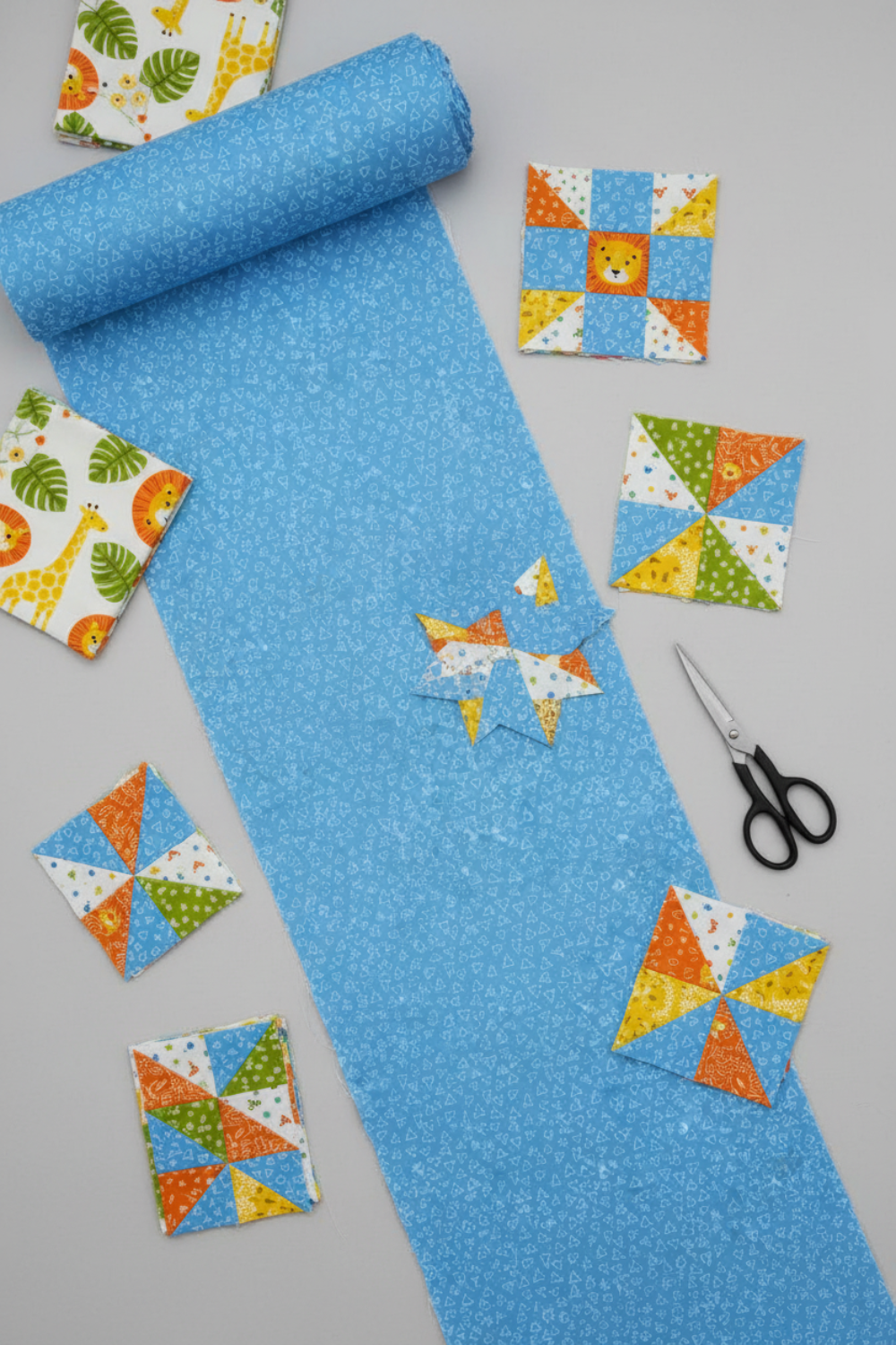 Safari Fun Floating Triangles Blue by Terry Runyan for Benartex – rolled fabric with coordinating pinwheel and star quilt blocks in progress, scissors, light grey background