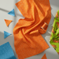 Safari Fun Floating Triangles Orange by Terry Runyan for Benartex – draped fabric with cut orange and blue triangle pieces, thread spool, and coordinating Tiger Too Lime fabric, natural window light