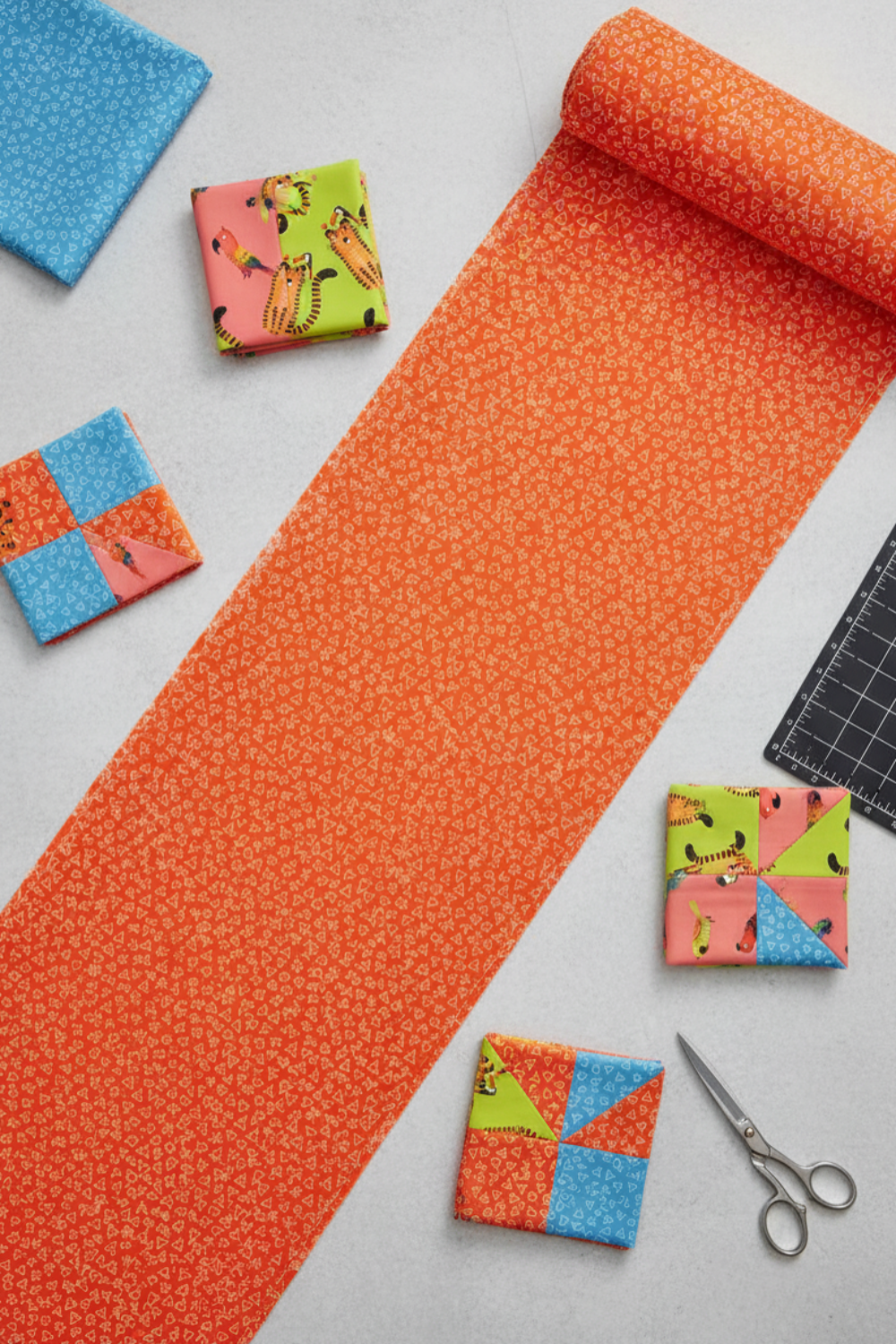 Safari Fun Floating Triangles Orange by Terry Runyan for Benartex – rolled fabric yardage with coordinating Safari Fun quilt blocks, scissors, and cutting mat, overhead view