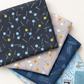 Vertical arrangement of folded coordinating fabrics in charcoal, gray, navy, and pale blue, topped with Bluish Pins & Buttons Charcoal.