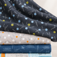 Bluish Pins & Buttons Charcoal fabric draped over a folded stack of coordinating gray, navy, and pale blue quilting fabrics.