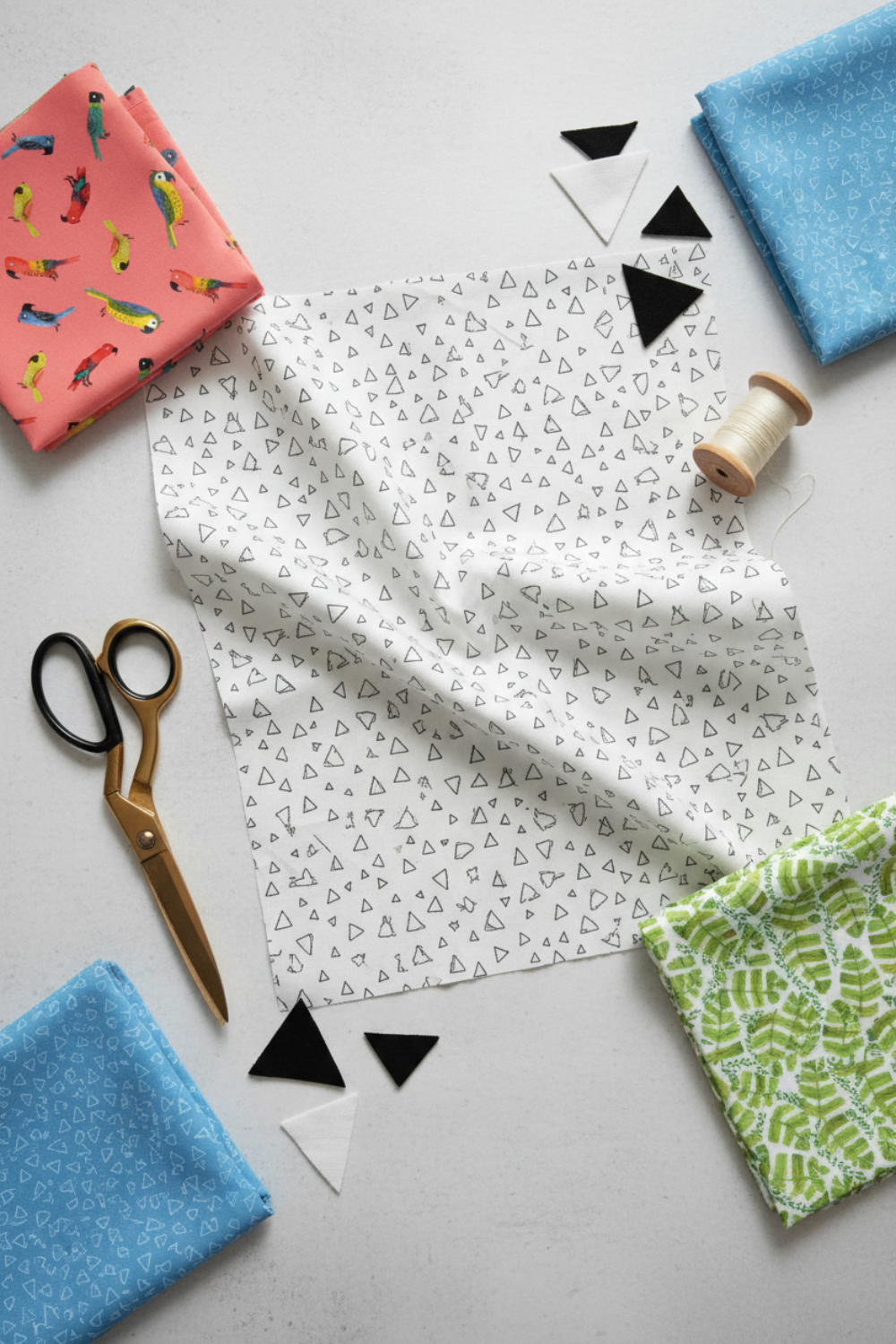 Safari Fun Floating Triangles White/Black by Terry Runyan for Benartex – overhead flat-lay with coordinating Jungle Birds and blue triangle fabrics, gold scissors, thread spool, and cut black and white triangle quilt pieces