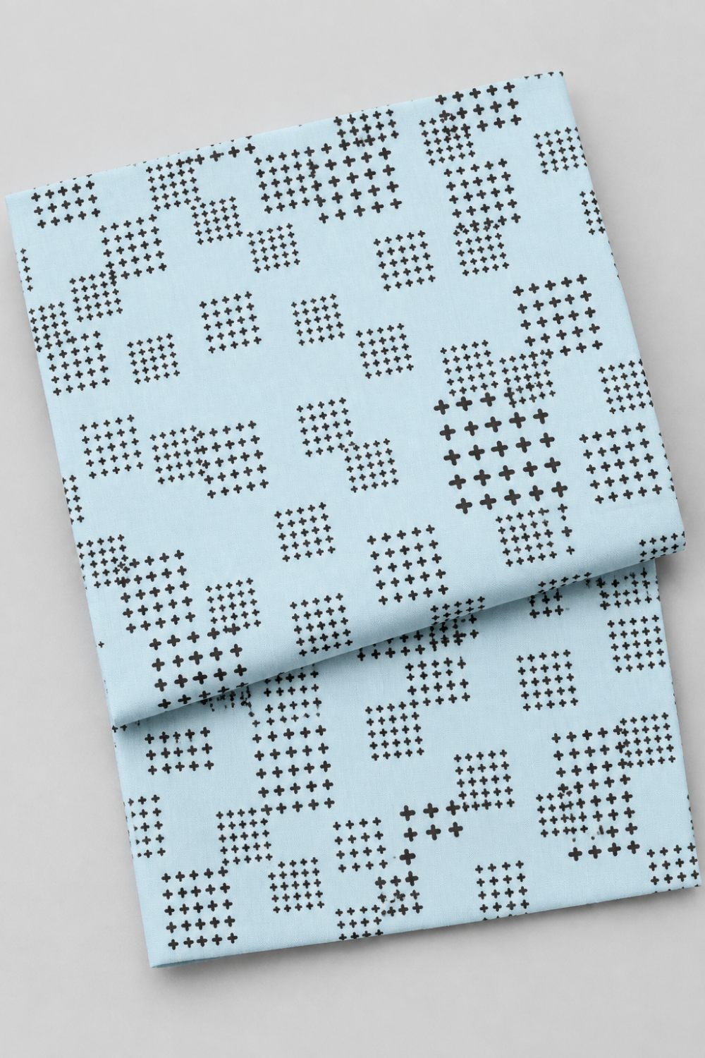 Folded Lazy Afternoon Sky Fabric by Zen Chic for Moda Fabrics on a light gray background, showing its pale blue print with scattered grids of black cross-shaped marks.