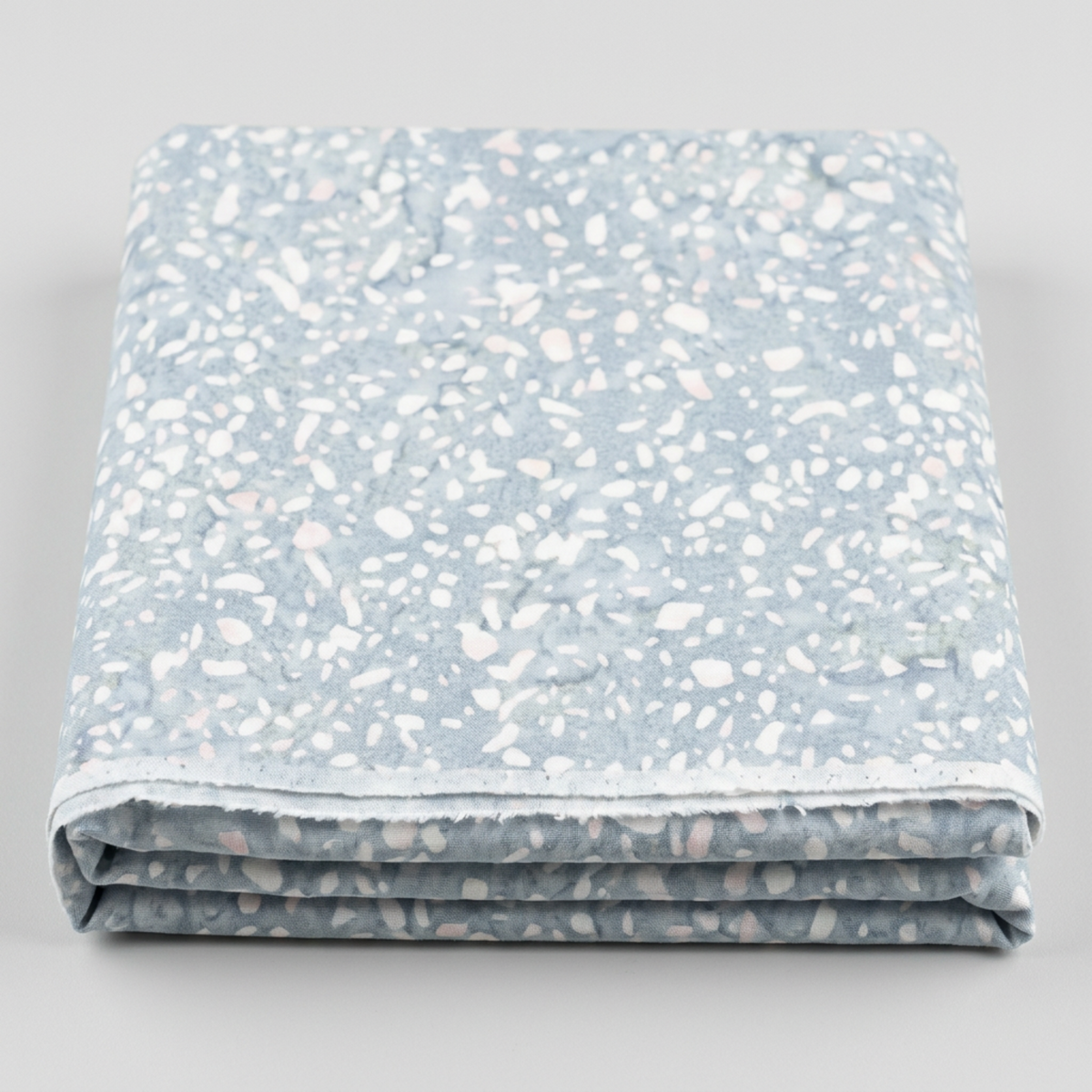 Terrazzo Powdered Pearl Fabric by Riley Blake Designs folded on a light-gray background, showing its pale pebble print and raw cut edge.