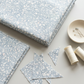 Folded Terrazzo Powdered Pearl Fabric by Riley Blake Designs beside matching triangular remnants, ivory thread spools, and a ceramic dish holding pins.