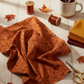 Prism II Rust Floral Vines 3 Yard Cut quilting cotton by Jason Yenter for In The Beginning Fabrics — loosely draped on a warm white wooden surface with coordinating mustard, butterscotch, burgundy, and warm brown fabric swatches, rust thread spools, gold scissors, dried autumn leaves, and a mug of tea in a warm cozy sewing room.