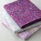 Terrazzo Purple Haze Fabric by Riley Blake Designs on top of a folded stack with coordinating pale blue-gray and pink-lilac fabrics.