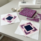 Two unfinished diamond-framed quilt blocks with Purple Haze accents beside folded fabric, remnants, pins, thread, and a sewing machine. Quilt blocks shown for inspiration feature the Quartzite Quilt Pattern by Bear Hug Quiltworks, available at IraRobi Quilts.