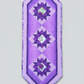 Bread and Butter Purple Twilight quilted table runner with three dark purple star blocks, floral centers, lavender borders and pointed ends on light gray.