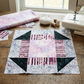 Quilt block with a Lilac Lustre center, plum striped bars, dark triangles, and gray botanical framing on a sewing table with fabric, remnants, thread, pins, and a sewing machine. Quilt blocks shown for inspiration. Coordinating fabrics and quilt patterns are available at IraRobi Quilts.