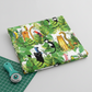 Safari Fun White/Multi quilting cotton partially folded on a light grey surface with a teal rotary cutter and corner of green cutting mat — large-scale jungle watercolor print by Terry Runyan for Benartex