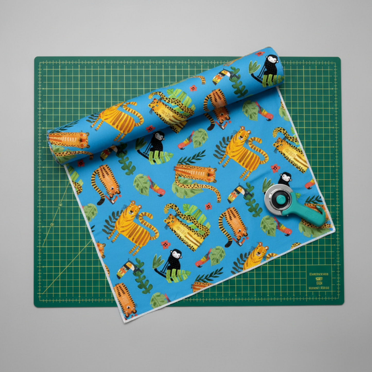 Safari Fun Playful Safari Blue quilting cotton partially unrolled on a green cutting mat with a teal rotary cutter — whimsical jungle animal print by Terry Runyan for Benartex