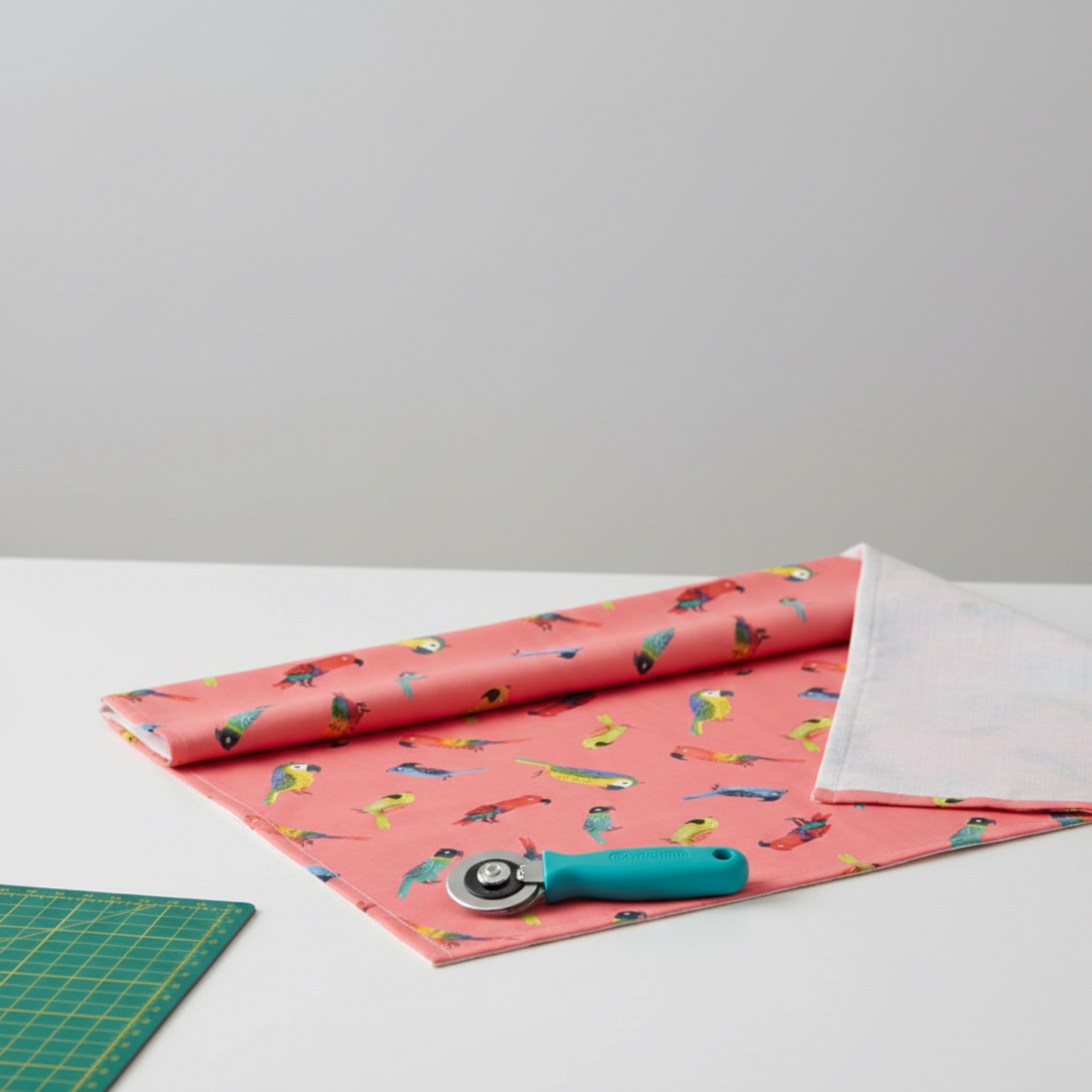 Safari Fun Jungle Birds Sorbet quilting cotton partially folded on a cutting mat with a rotary cutter — coral parrot print by Terry Runyan for Benartex