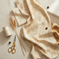 Reflections of Autumn II Twigs 3 Yard Cut quilting cotton by Jason Yenter for In The Beginning Fabrics — shown with coordinating warm cream, taupe, and honey gold fabric swatches, cream thread spool, gold scissors, and dried wheat stalks in a soft organic flat lay.