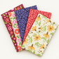Coordinating Superbloom fabrics by Robin Pickens for Moda Fabrics, arranged in a fan with golden-yellow Daisyish flowers on cream beside coral and indigo leafy prints and cream and burgundy florals.