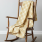 Golden Era by Paula Barnes, Floral Plaid Tan for Marcus Fabrics — warm tan-gold quilting cotton with diagonal lattice and cream floral wreath motifs draped over a rustic rocking chair — IraRobi Quilts
