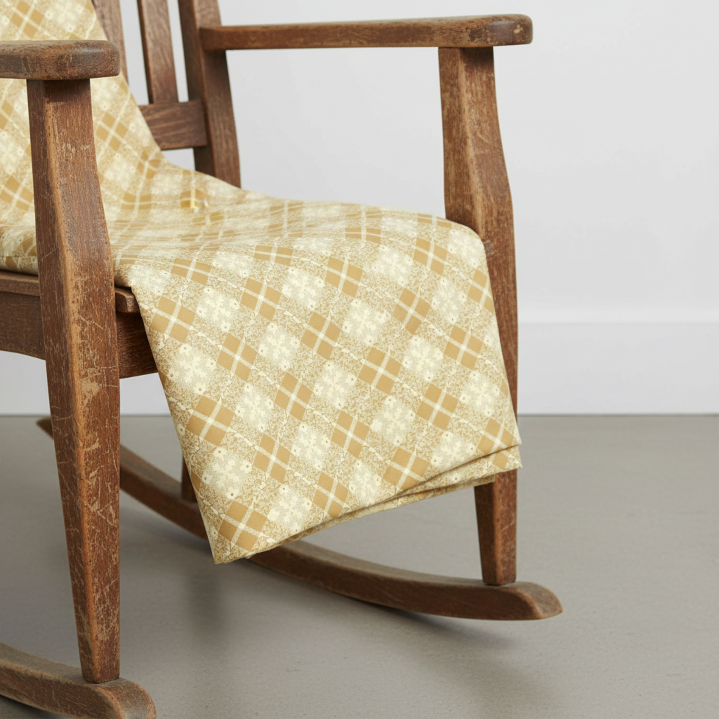 Golden Era Floral Plaid Tan quilting cotton by Paula Barnes for Marcus Fabrics — fabric draped over a rustic wooden rocking chair showing natural drape and warm tan-gold diagonal lattice floral wreath print