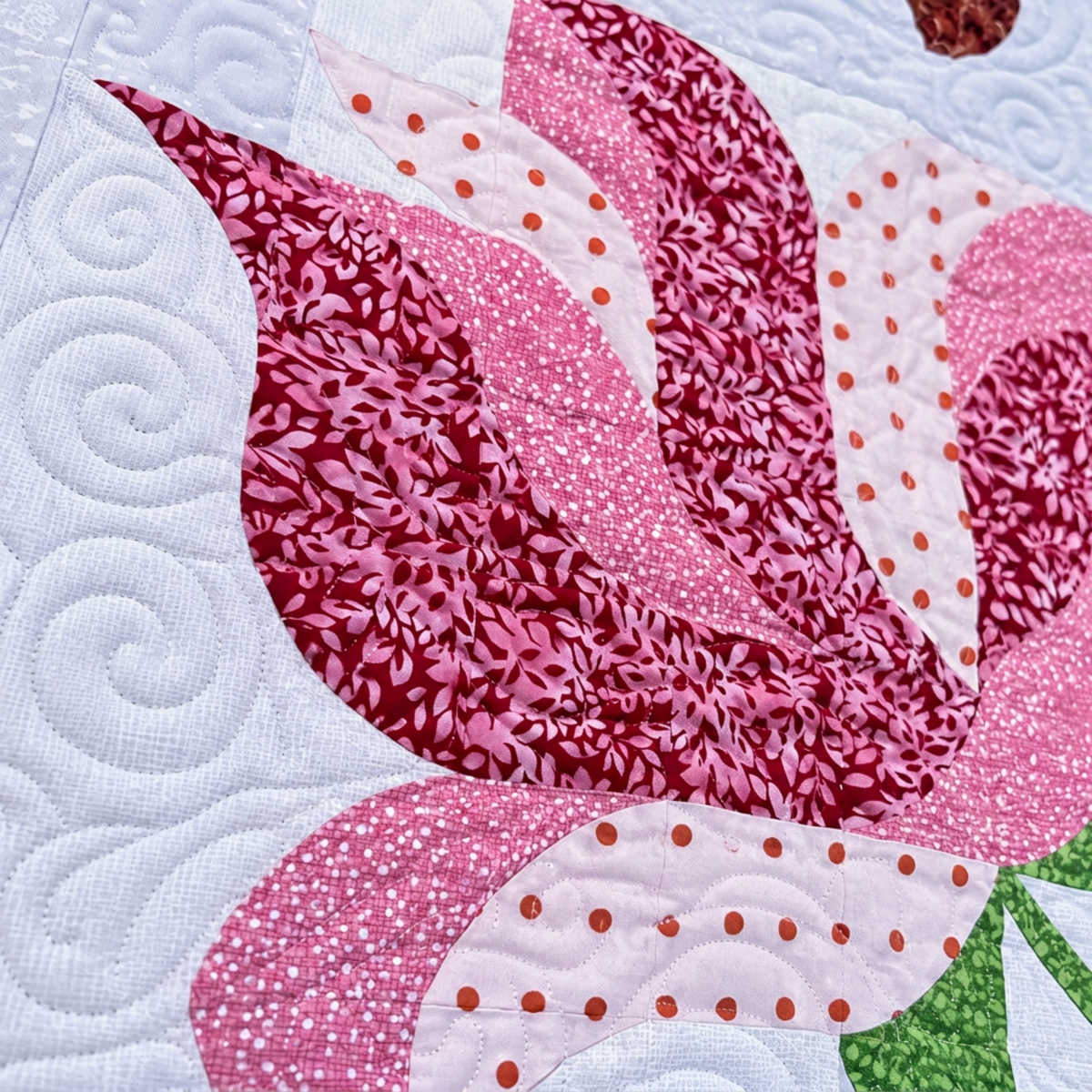 Alt text: Detail of a Rose Garden quilt block with pink and burgundy leaf prints, orange-dotted fabric, curved seams, and spiral quilting.