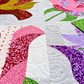 Close-up of Rose Garden quilt showing pink and purple curved patchwork, green leaves, pale printed fabrics, and spiral quilting.