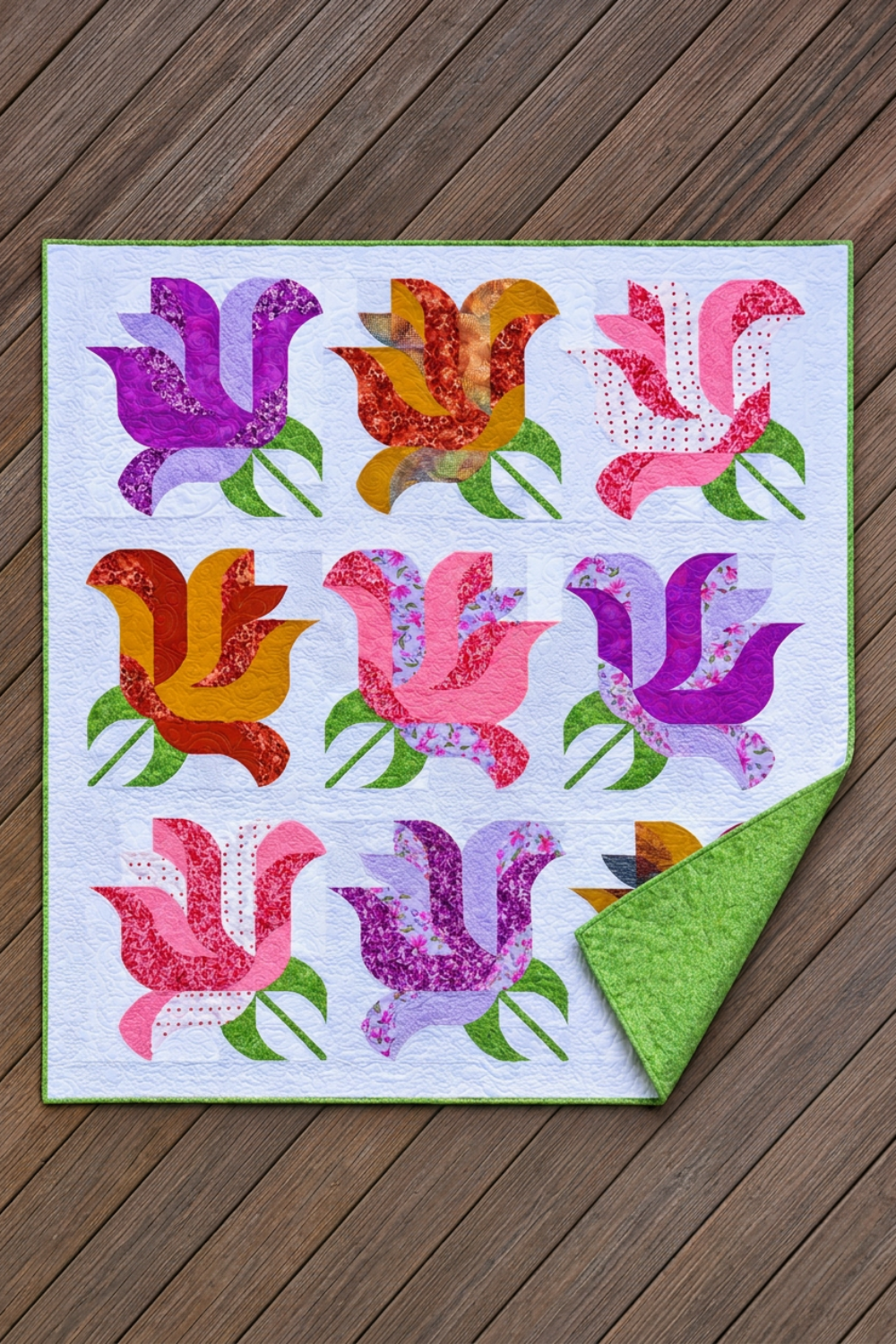 Rose Garden quilt on wooden decking with a corner folded back to reveal its green patterned backing and coordinating binding.