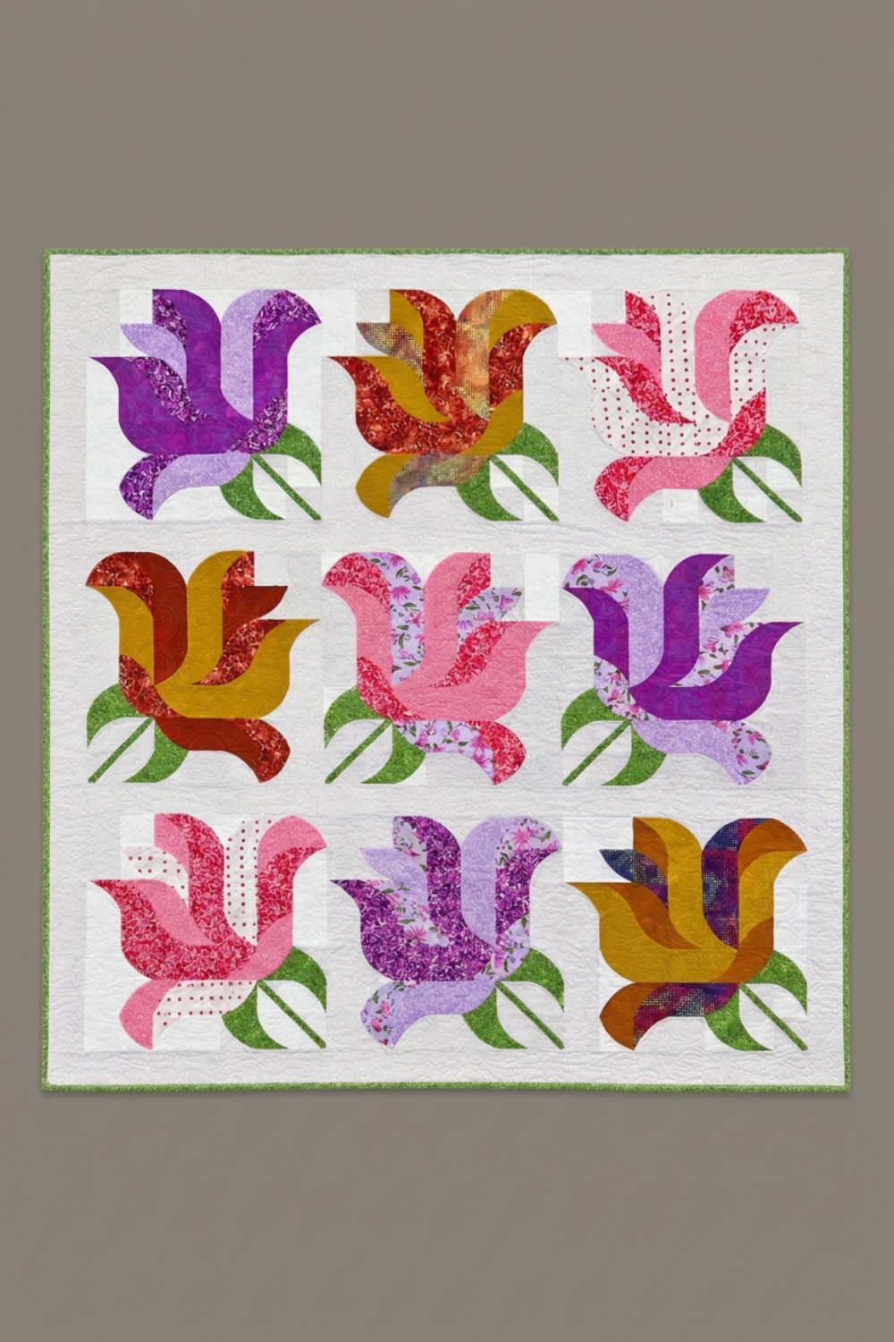 Rose Garden handmade quilt with nine pink, purple, and golden-toned rose blocks, green leaves, and green binding on a warm grey background.