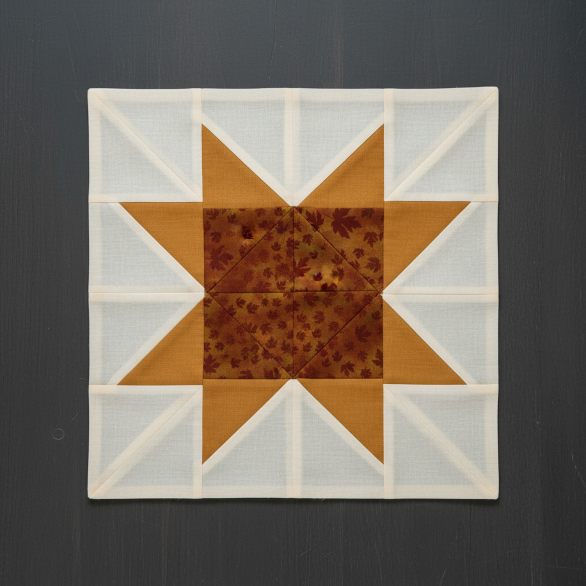 Autumn Celebration Brown Maple Leaves fabric by Jason Yenter for In The Beginning Fabrics used in quilt block star points and center diamond — tossed dark burgundy maple leaf silhouettes on mottled amber and rust ground, paired with soft golden amber accent squares on cream background. Quilts shown for inspiration. Coordinating fabrics and quilt patterns available at IraRobi Quilts.
