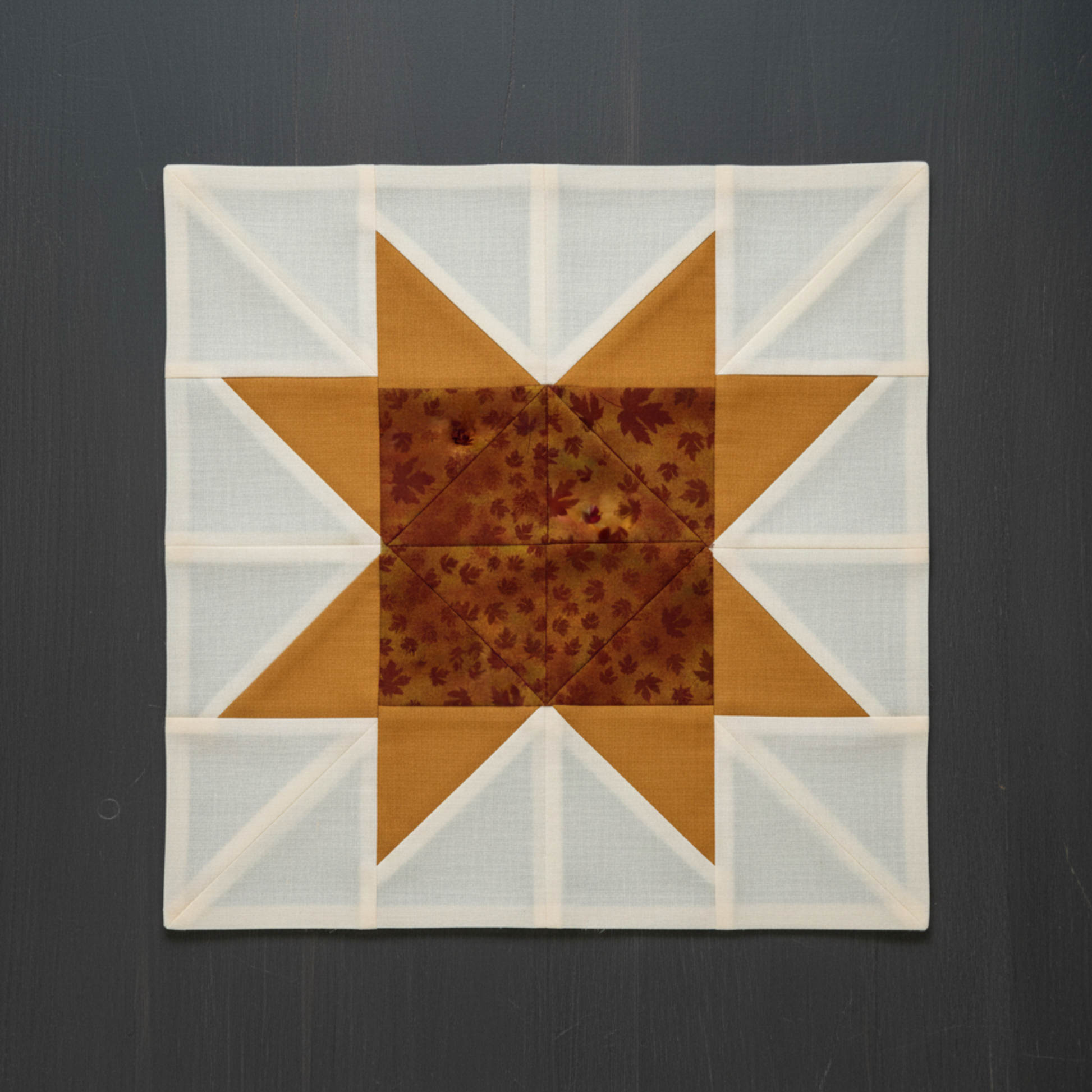 Autumn Celebration Brown Maple Leaves fabric by Jason Yenter for In The Beginning Fabrics used in quilt block star points and center diamond — tossed dark burgundy maple leaf silhouettes on mottled amber and rust ground, paired with soft golden amber accent squares on cream background. Quilts shown for inspiration. Coordinating fabrics and quilt patterns available at IraRobi Quilts.