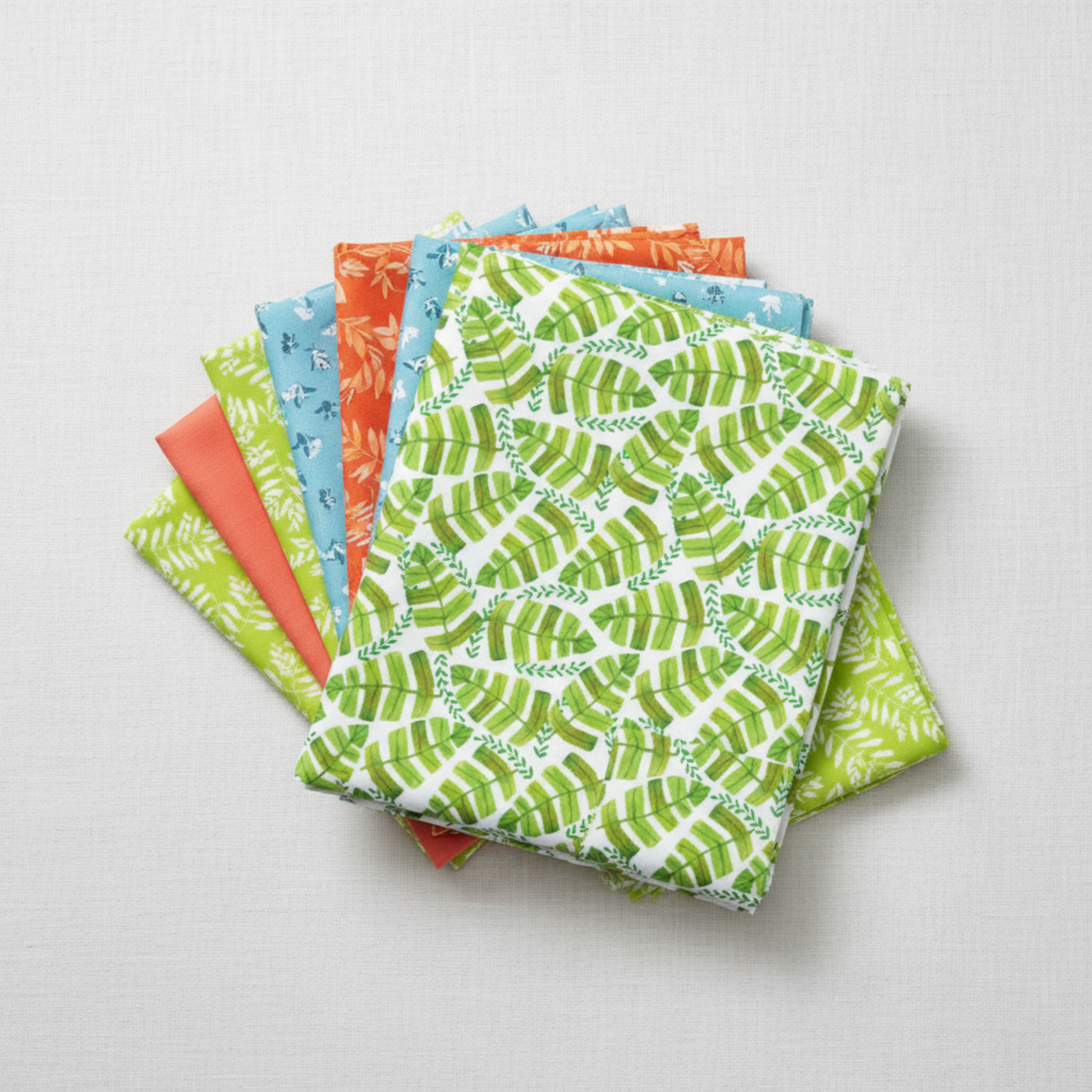 Safari Fun Jungle Leaves White by Terry Runyan for Benartex shown in a coordinating fabric stack with prints in coral sorbet, orange, cornflower blue, and lime green. Quilt blocks shown for inspiration. Coordinating fabrics and quilt patterns are available at IraRobi Quilts.